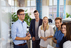 6 junge Leute mit legerer Arbeitskleidung stehen zusammen in einem modernen Großraumbüro.